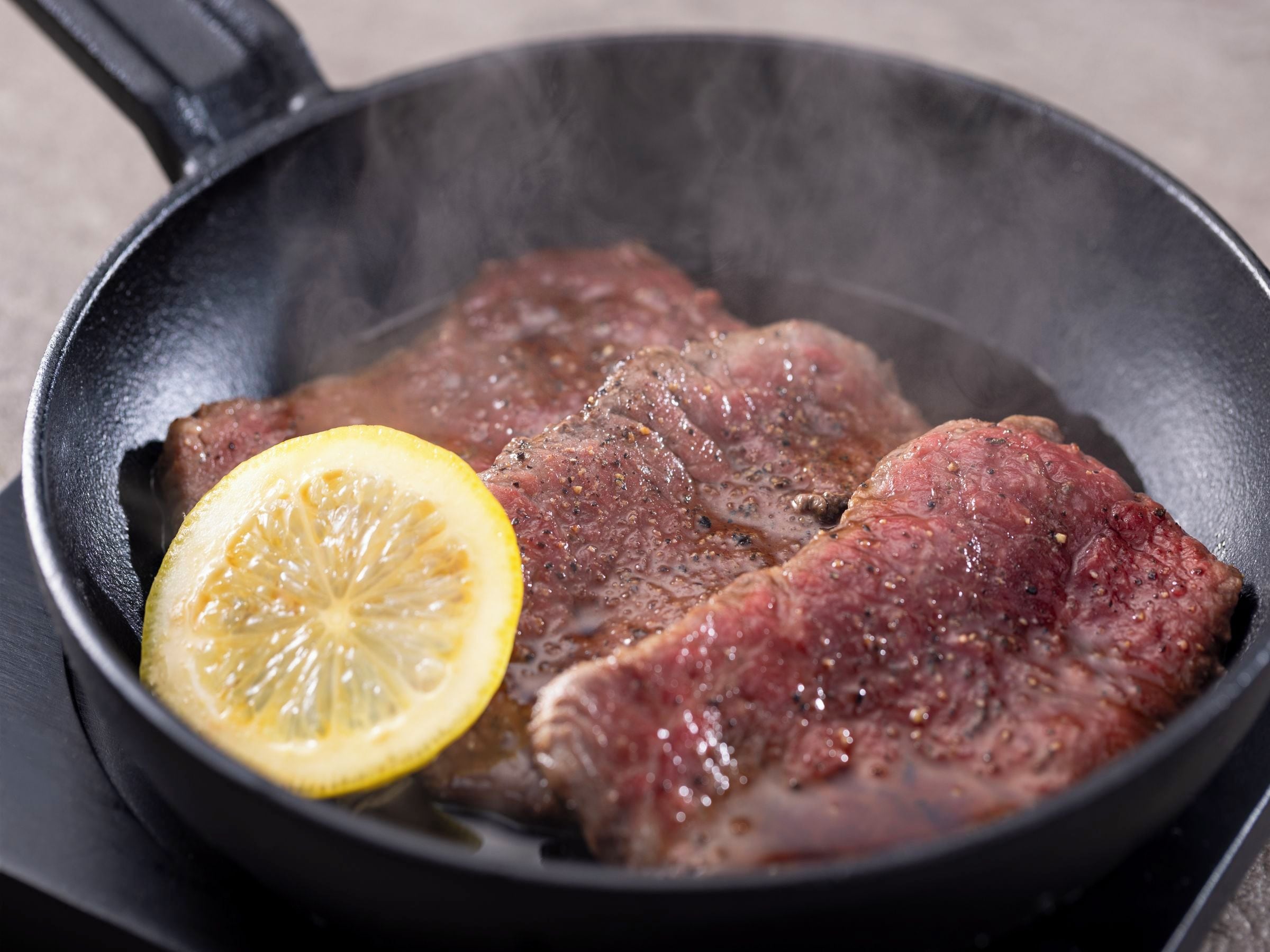 Uma frigideira com duas fatias de carne e uma fatia de limão.