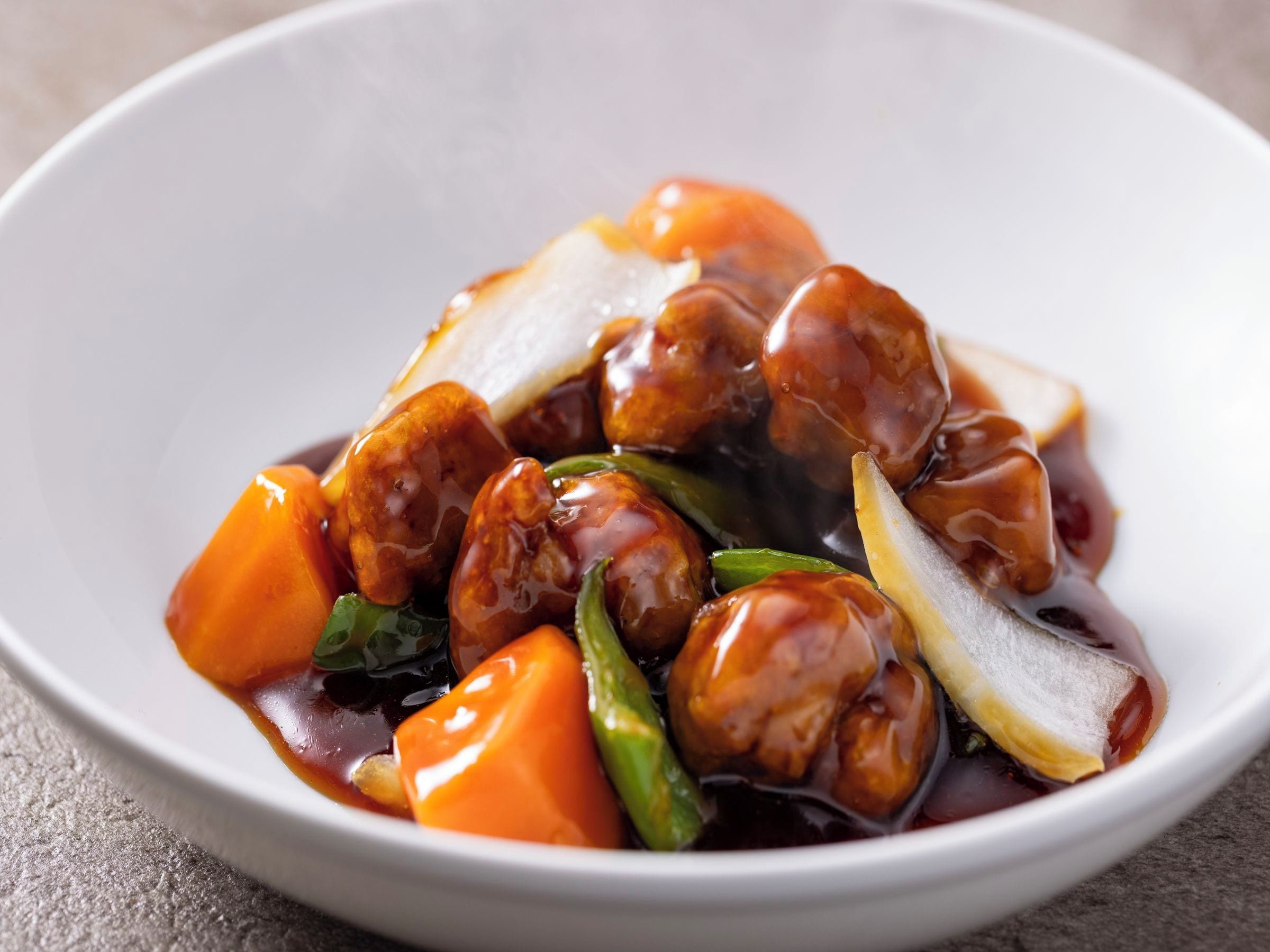 A bowl of food with a glossy sauce, containing pieces of meat and vegetables.