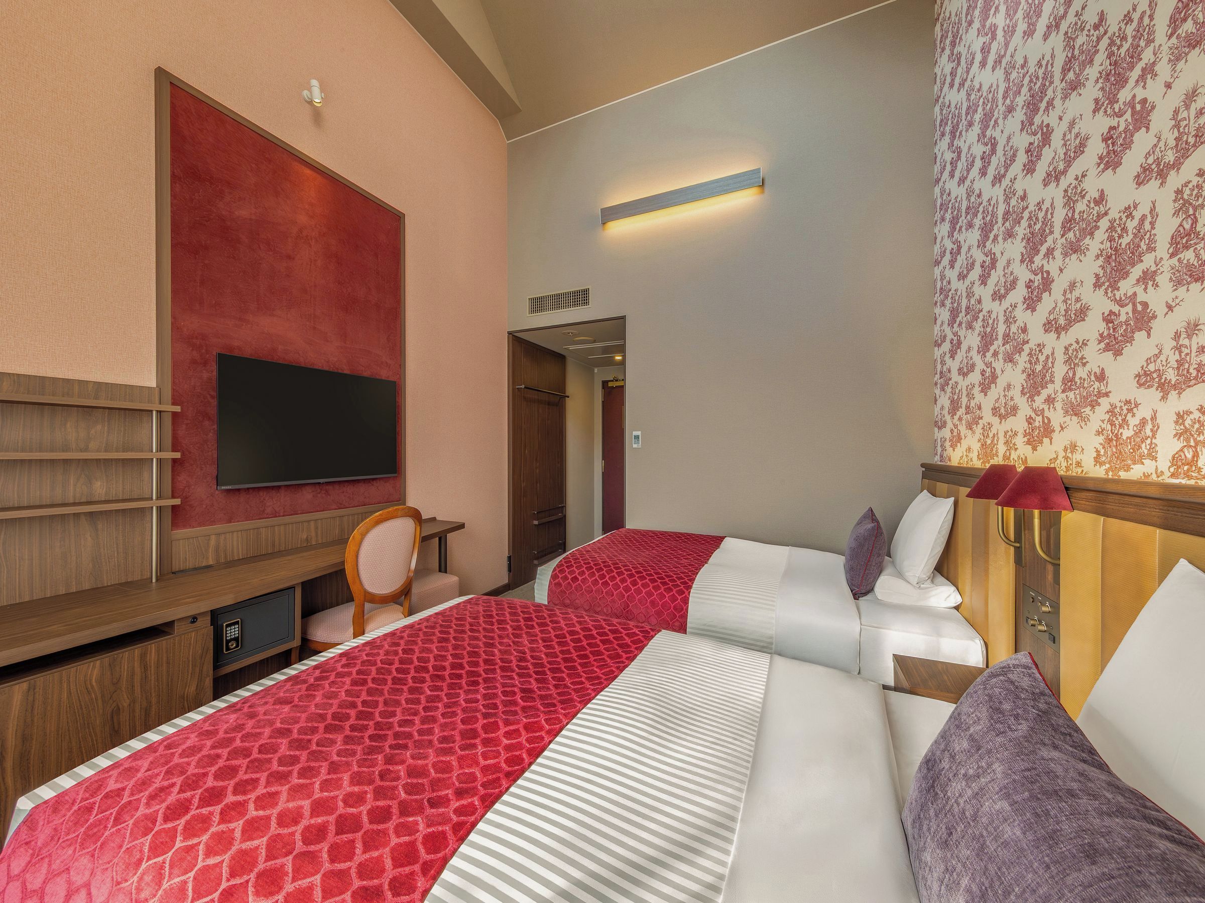 A hotel room with a large bed, a television, a desk, and a wardrobe.