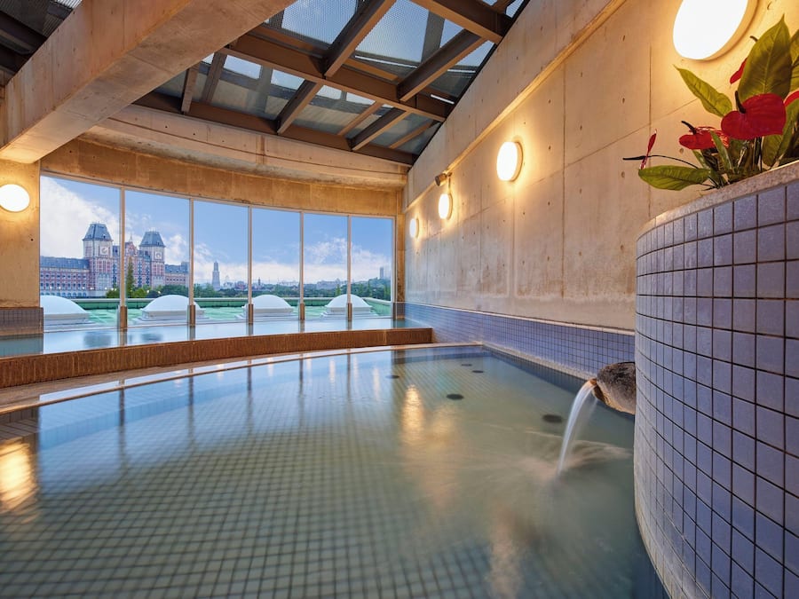 A swimming pool with a view of a cityscape, large windows, and a tiled wall.