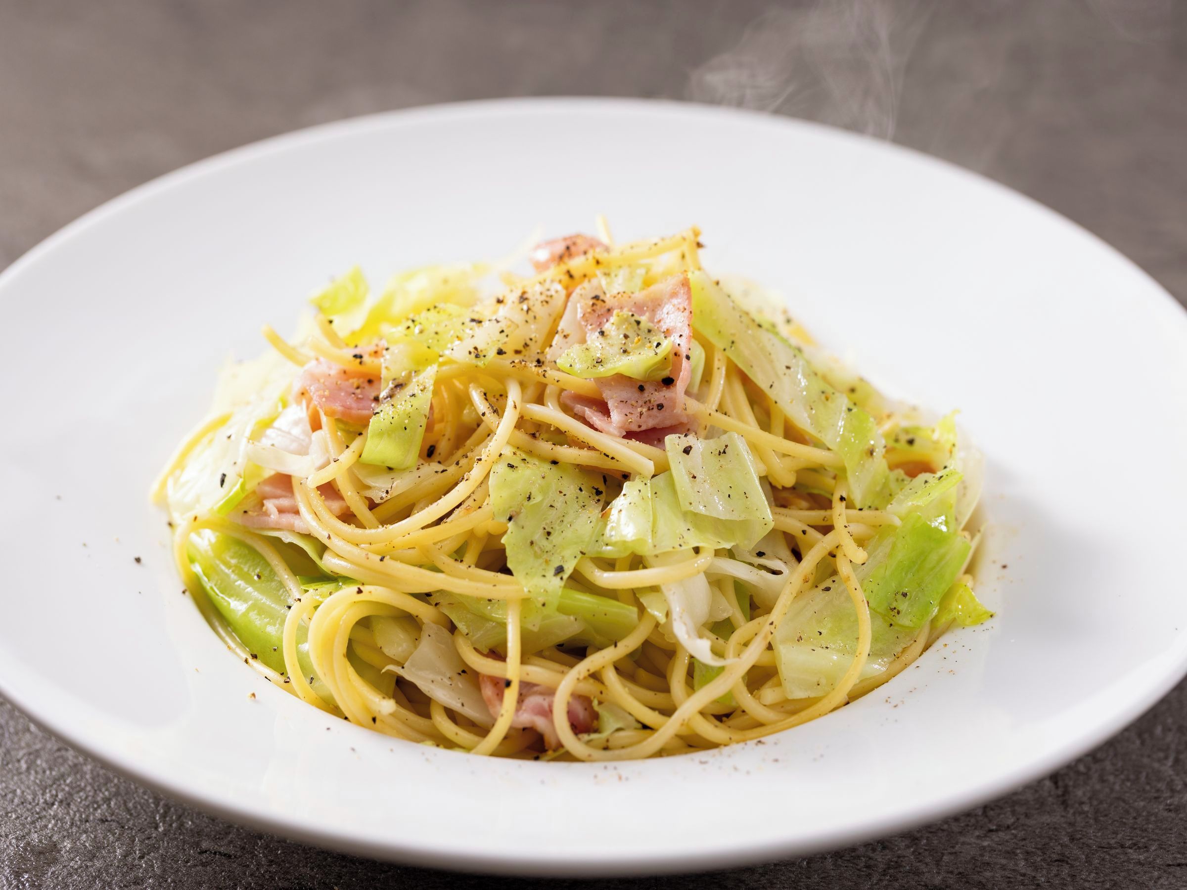 A plate of spaghetti with vegetables and ham.