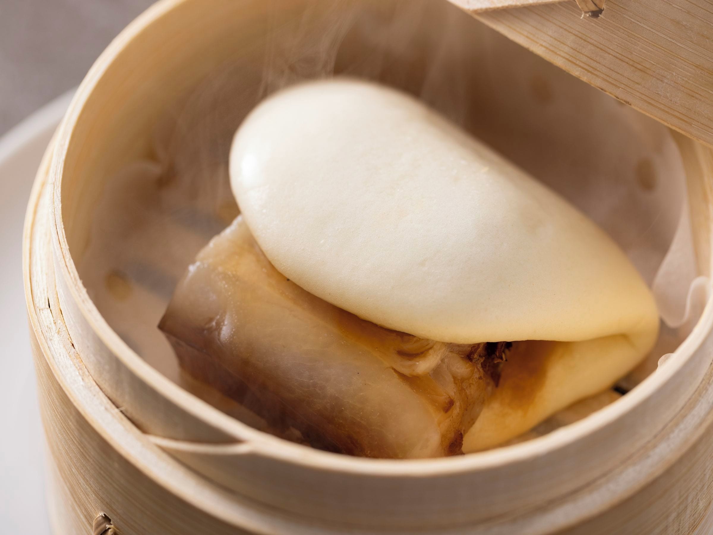 A bamboo steamer with a white lid, containing a food item.