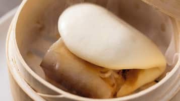 A bamboo steamer with a white lid, containing a food item.