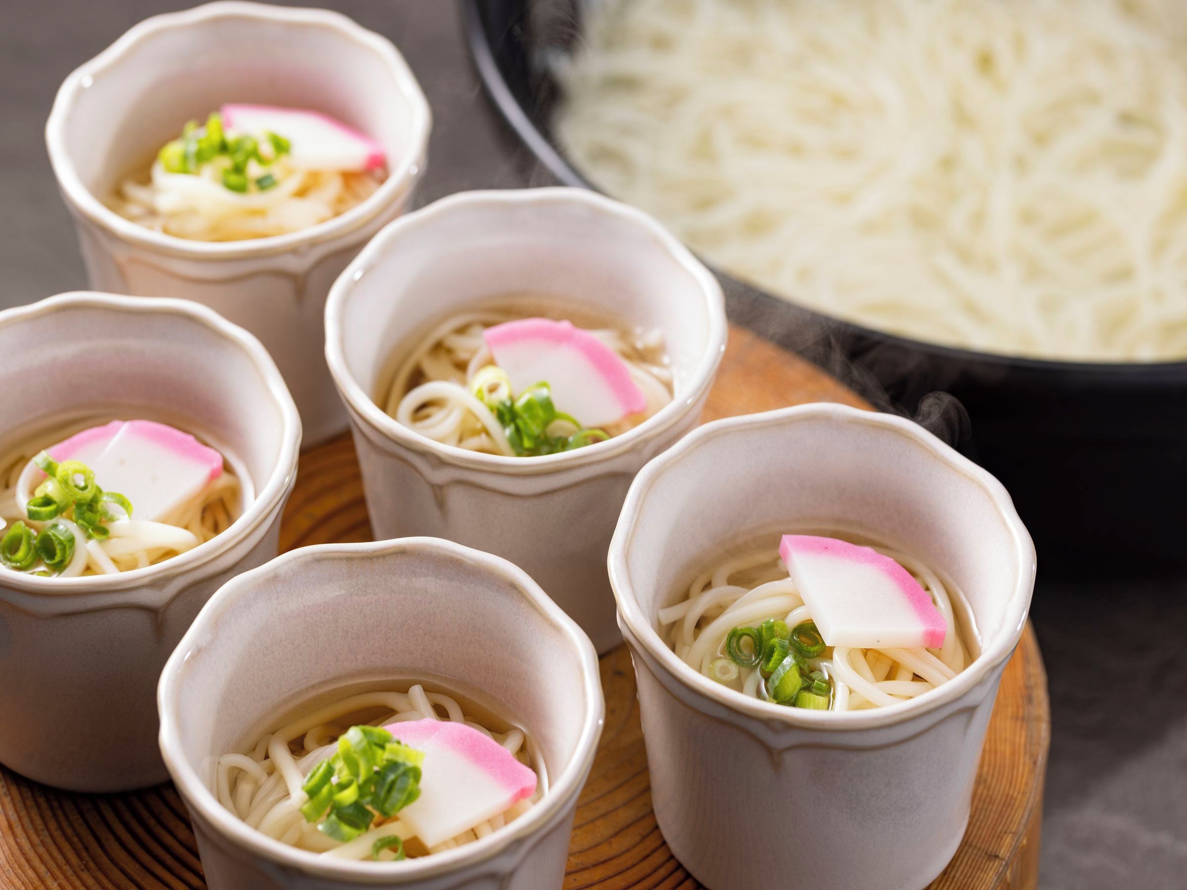 Four bowls of ramen with toppings, a bowl of noodles, and a pot in the background.