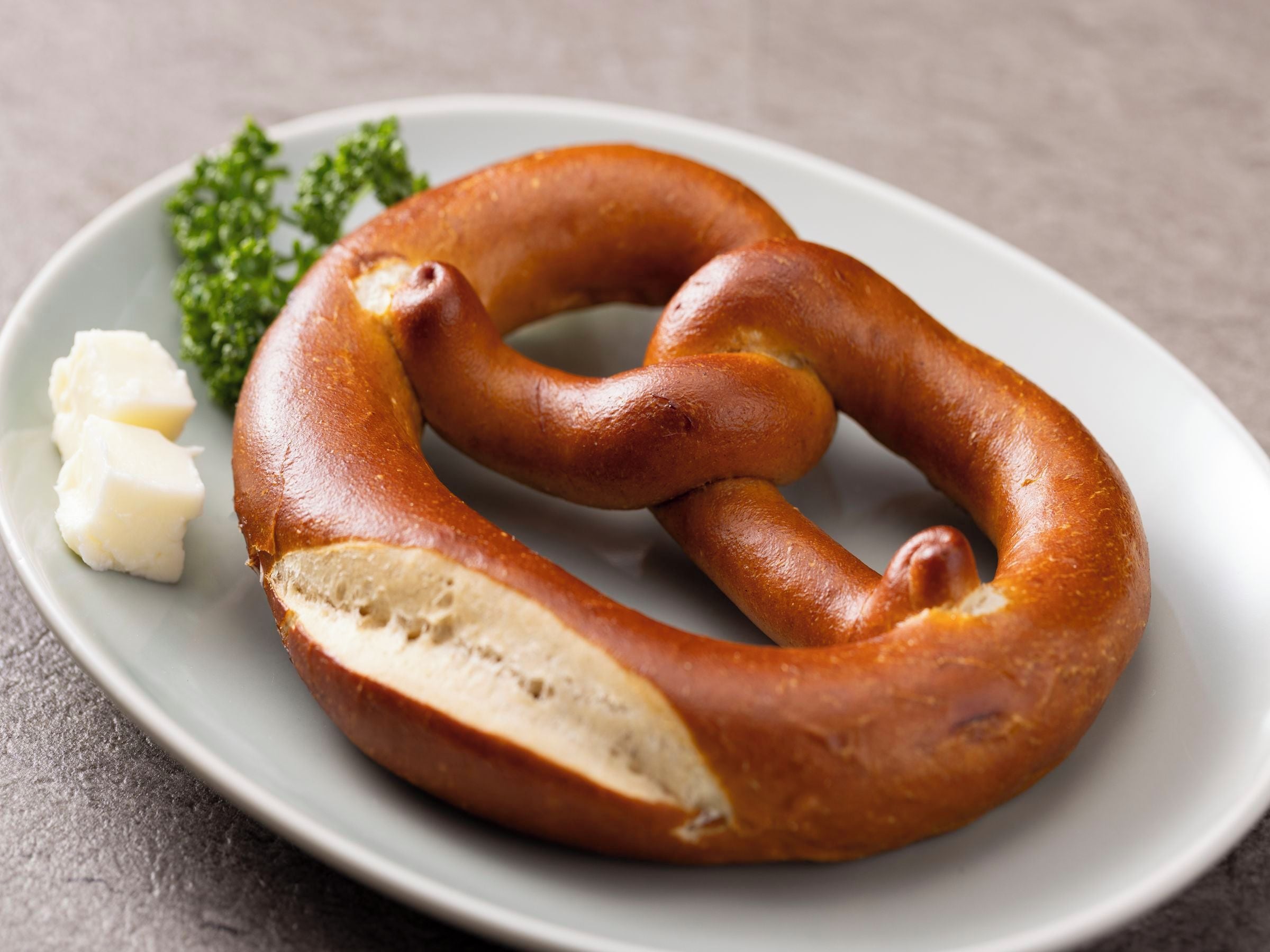 A pretzel with a visible cut section, accompanied by a small portion of butter and parsley on a plate.