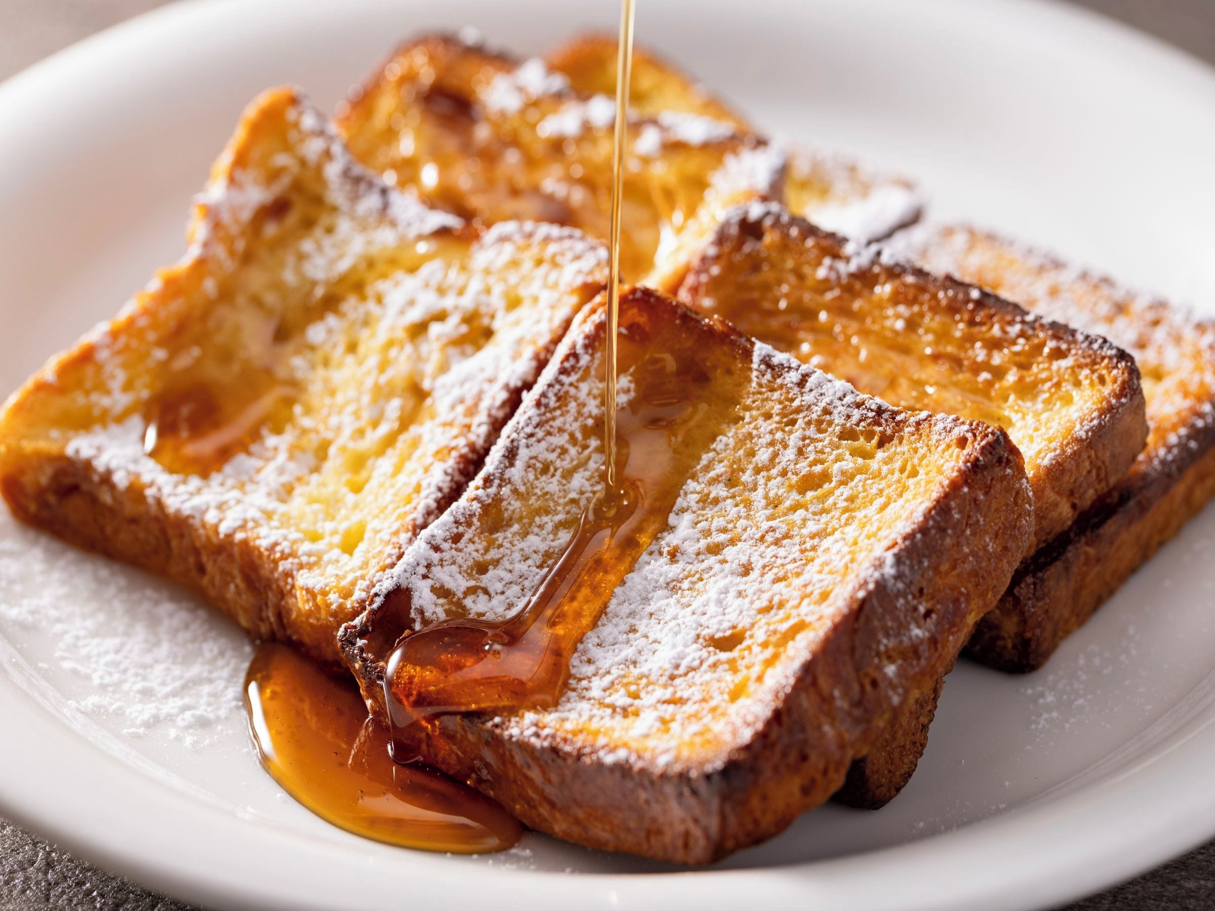 A plate of French toast with syrup and powdered sugar.