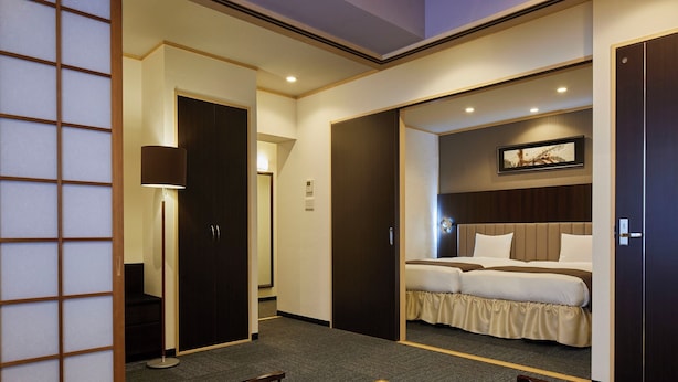 Camera d'albergo con un letto, una scrivania e una sedia. Si apre una porta verso un'altra stanza.