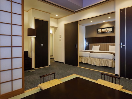 A hotel room with a bed, a desk, and a chair. There is a door leading to another room.