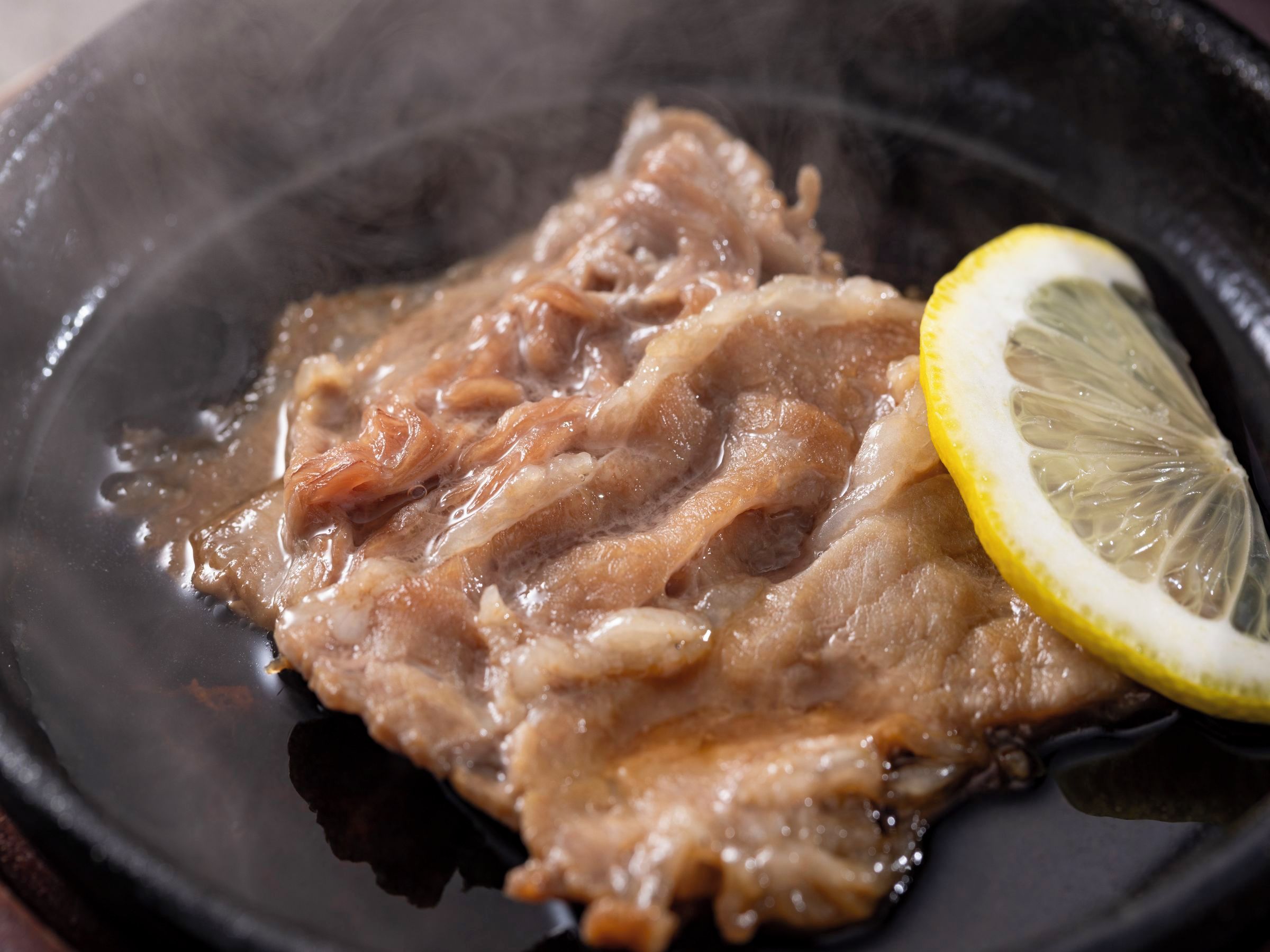 A close-up of a cooked meat dish in a pan with a slice of lemon on the side.