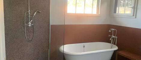A bathroom with a freestanding bathtub, a shower enclosure, and a window providing natural light.