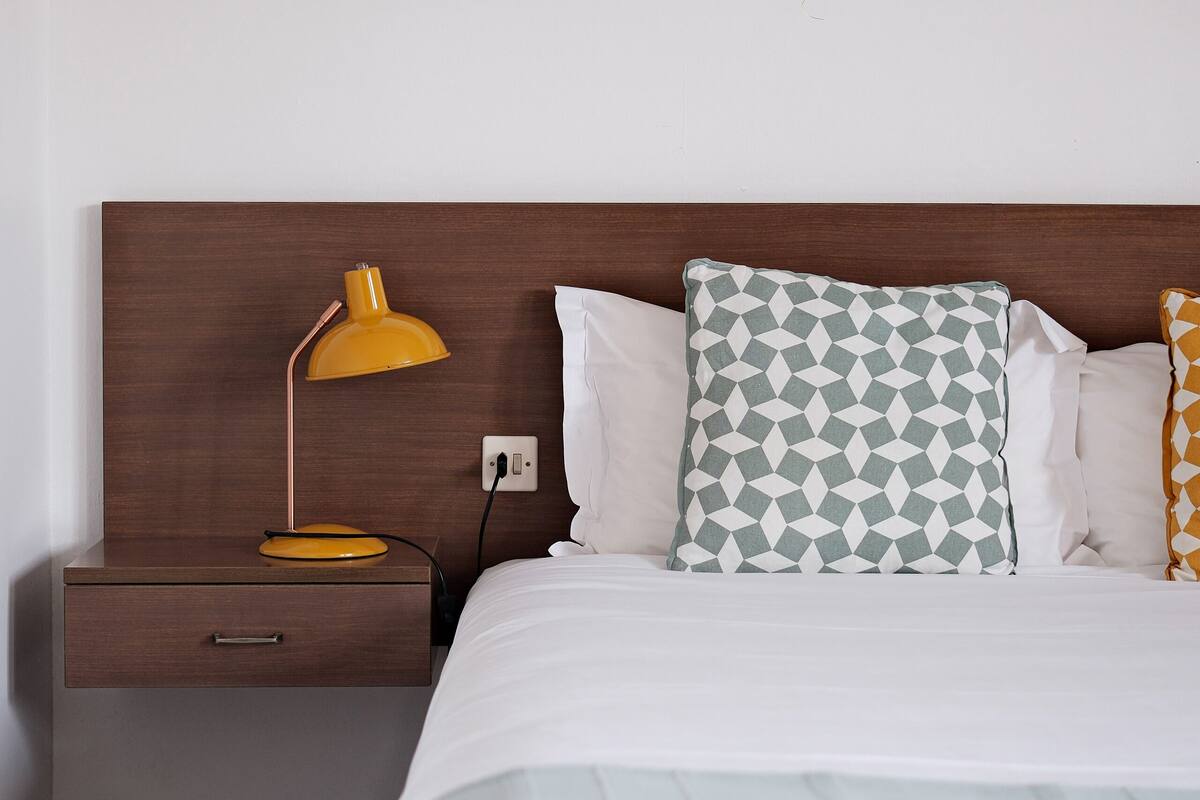 Un lit bien fait, avec un oreiller à motifs, une lampe de chevet et une tête de lit en bois.