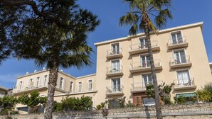 A multi-story building with balconies, a stone wall, and a palm tree. - Résidence Le Beau Rivage (Bandol)