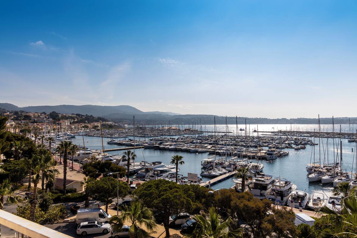 Un port de plaisance où sont amarrés de nombreux bateaux, entouré de verdure et de bâtiments.