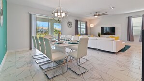 A modern living room with a white sofa, a dining table with chairs, a TV, and a ceiling fan. - ChampionsGate, 9 Bed Luxury Exec Villa, Sleeps 26, Pool & Spa Heat Included (ChampionsGate)
