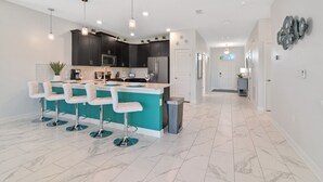 A modern kitchen with a central island, bar stools, dark cabinets, stainless steel appliances, and a tiled floor. - ChampionsGate, 9 Bed Luxury Exec Villa, Sleeps 26, Pool & Spa Heat Included (ChampionsGate)