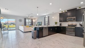 A modern kitchen with dark cabinets, stainless steel appliances, and a large island. - ChampionsGate, 9 Bed Luxury Exec Villa, Sleeps 26, Pool & Spa Heat Included (ChampionsGate)