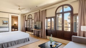 A hotel room with a bed, a desk, a TV, a window with curtains, and a view of buildings. - H10 Palacio Colomera (Córdoba)