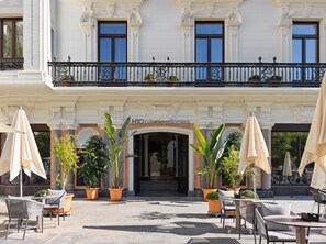 A hotel entrance with a balcony, outdoor seating, and potted plants. - H10 Palacio Colomera (Córdoba)