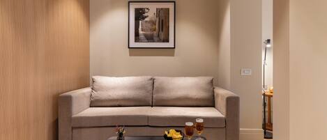 A modern living room with a sofa, a coffee table with drinks and snacks, and a framed picture on the wall.
