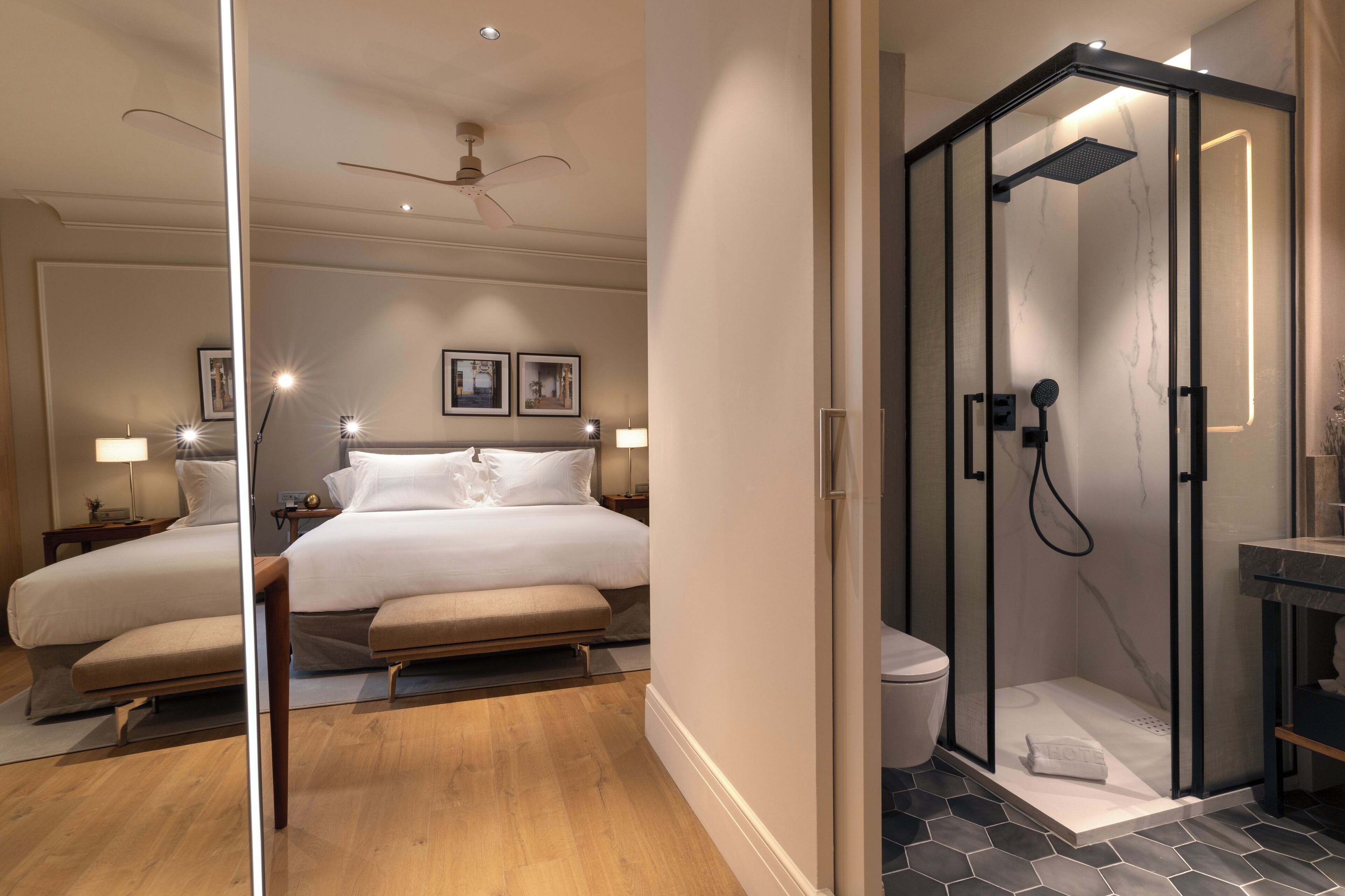 A modern hotel room with a large bed, a separate shower area, and a small bathroom.