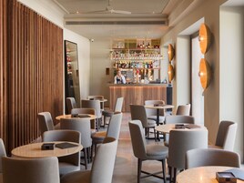 Eine moderne Bar mit einer Auswahl an Spirituosenflaschen und Gläsern, einer Theke und Sitzgelegenheiten mit runden Tischen und Stühlen.