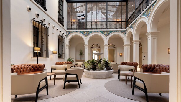 A spacious lobby with high ceilings, arched columns, and a central seating area with sofas and chairs. - H10 Palacio Colomera (Córdoba)