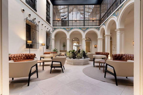 A spacious lobby with high ceilings, arched columns, and a central seating area with sofas and chairs. - H10 Palacio Colomera (Córdoba)