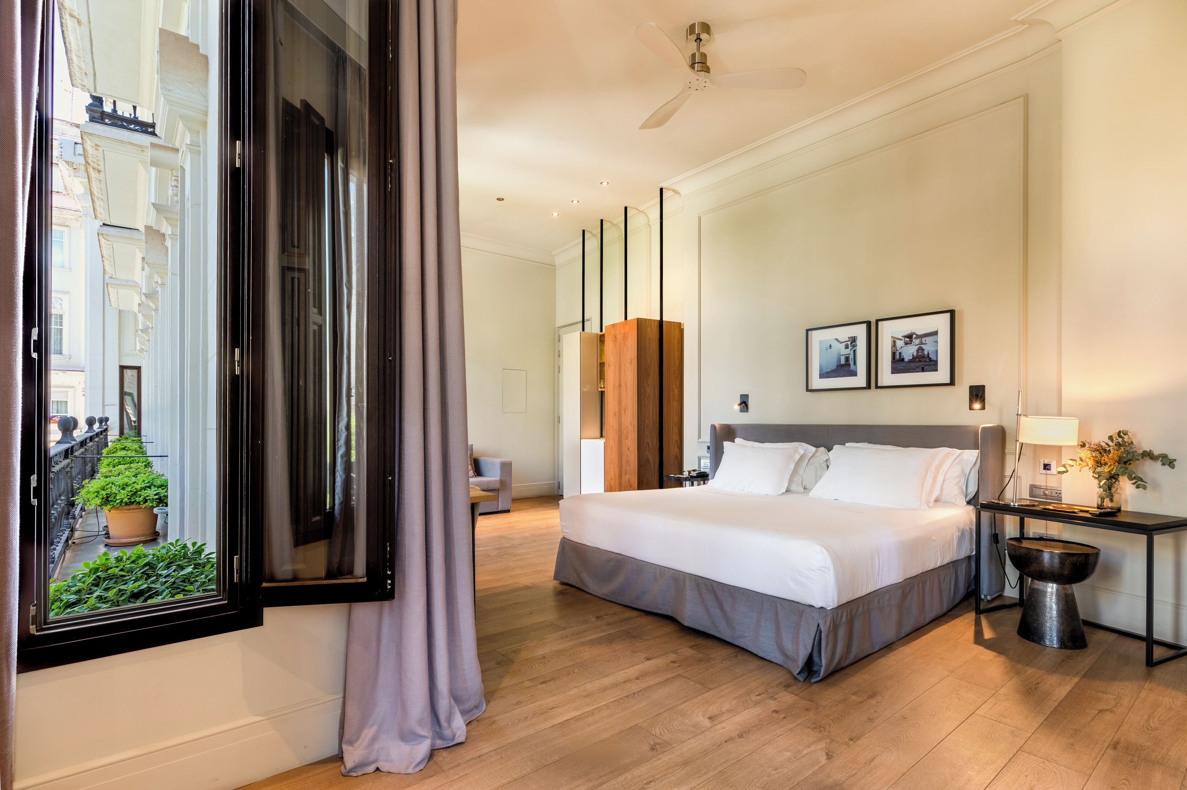 Une chambre d’hôtel avec un grand lit, un bureau avec une lampe, une petite table et une plante en pot.