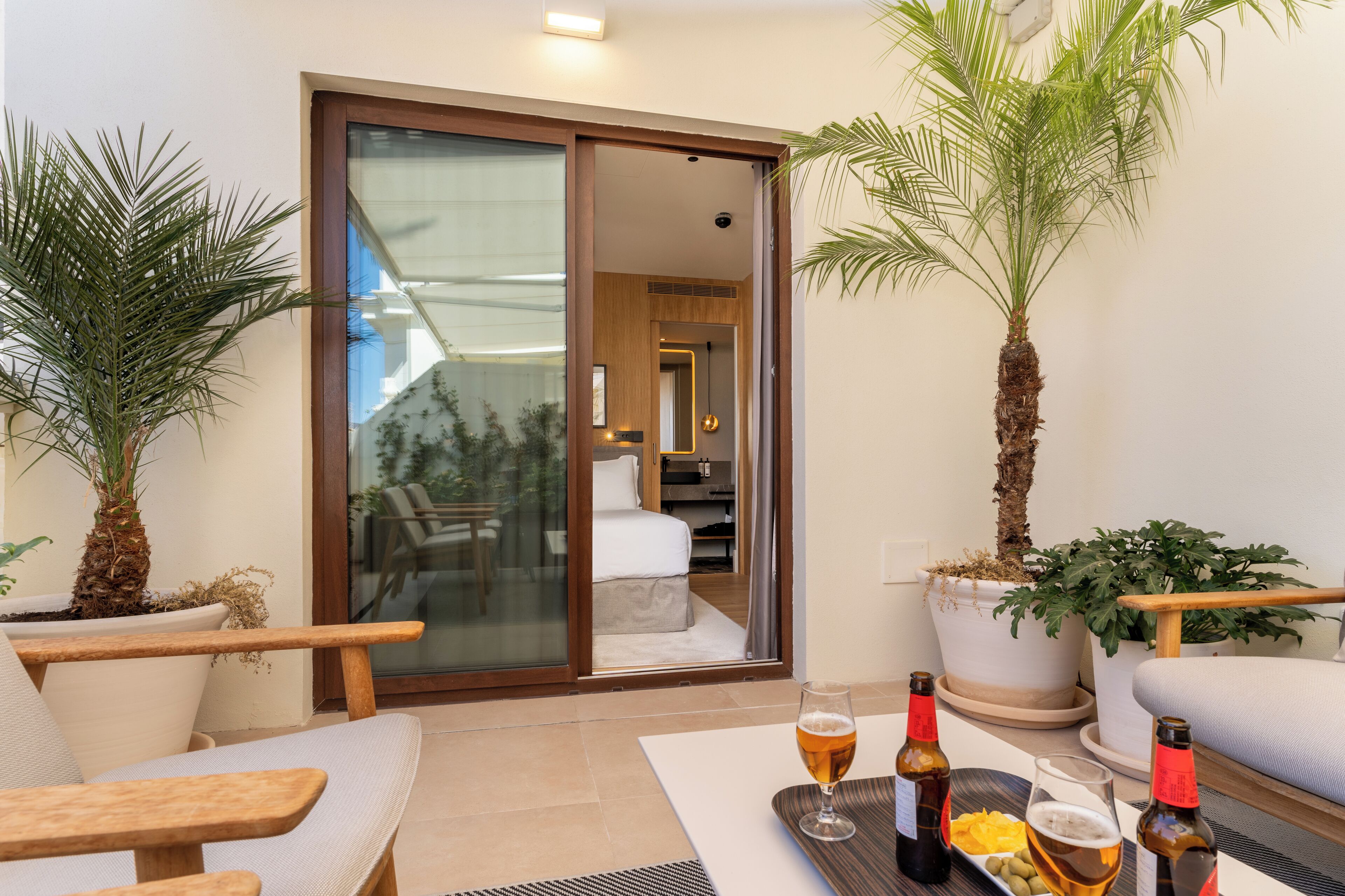 Habitación moderna con puerta de vidrio que da a un balcón, amueblada con sofá, sillas y una mesa de comedor con bebidas.