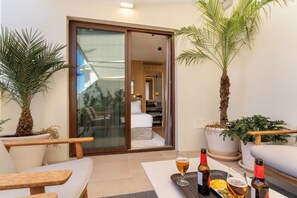 A modern room with a glass door leading to a balcony, furnished with a sofa, chairs, and a dining table with drinks. - H10 Palacio Colomera (Córdoba)