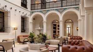 A spacious lobby with a high ceiling, a central fountain, and a seating area with leather sofas and armchairs. - H10 Palacio Colomera (Córdoba)
