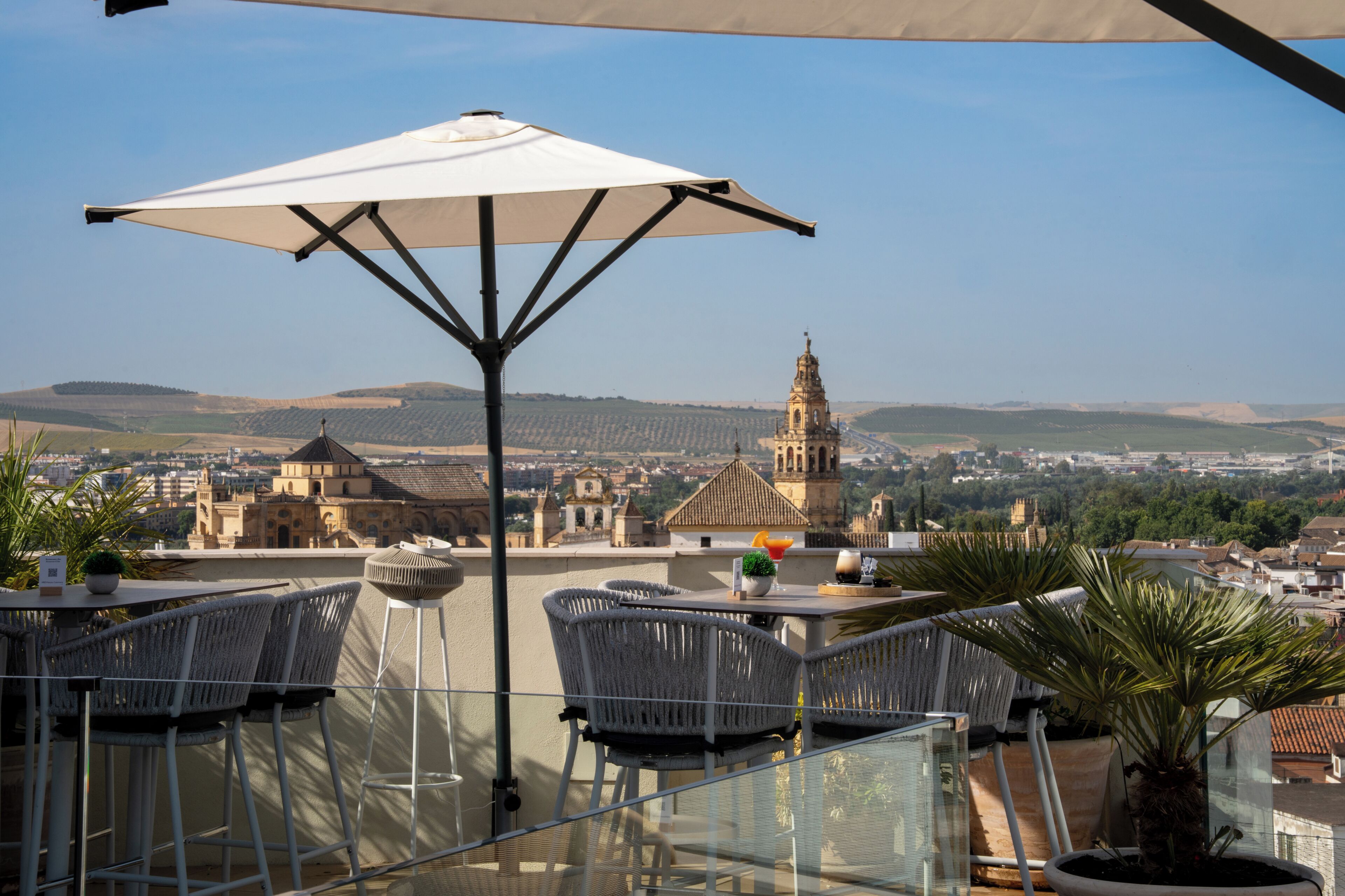 Um terraço com mesa e cadeiras, com vista para um horizonte urbano repleto de edifícios históricos e uma torre.