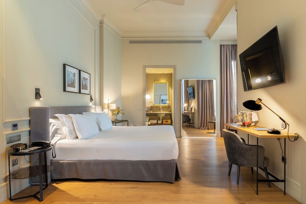 A hotel room with a large bed, a desk with a chair, a flat-screen TV, and a bathroom visible through an open door.