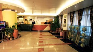 A hotel reception area with a reception desk, a TV screen, potted plants, and a display of sports balls. - Hotel La Vinci (Dhaka)