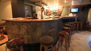 A bar area with a marble counter, stools, and a television screen. - Hotel La Vinci (Dhaka)