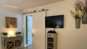 Une pièce avec un plancher en bois, un téléviseur fixé au mur, une porte blanche et un petit meuble avec des paniers.