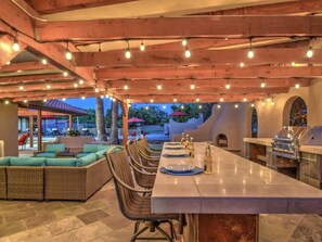 Un espace extérieur aménagé pour les repas, avec une longue table, des meubles en osier et un barbecue.