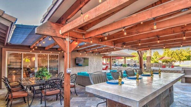 Een terras buiten met een stenen vloer, een houten pergola en zitplaatsen.
