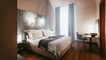 A modern hotel room with a large bed, bedside table, and a desk with a chair.