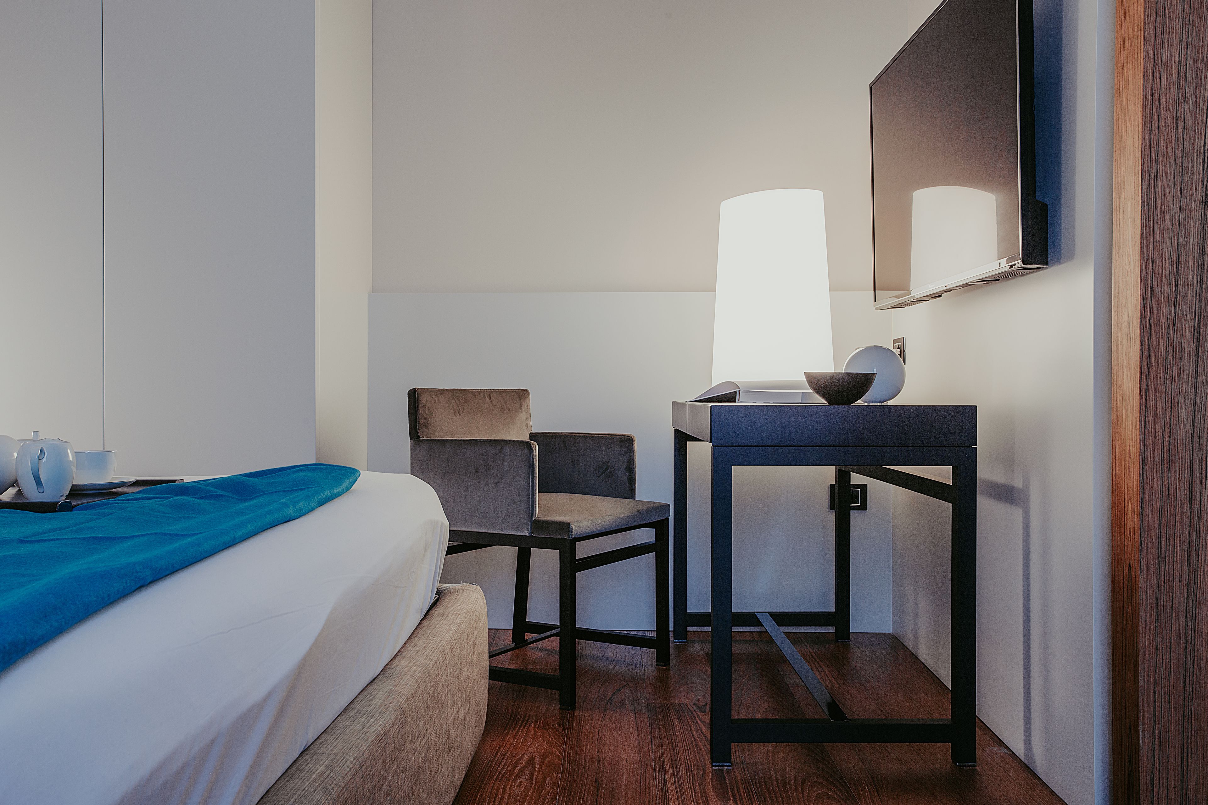 Una habitación de hotel con cama, escritorio, silla, lámpara y espejo.