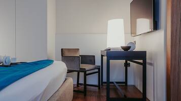 Una habitación de hotel con cama, escritorio, silla, lámpara y espejo.