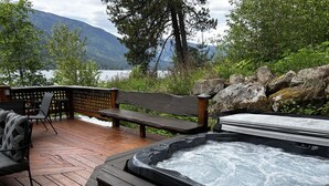 Une terrasse en bois avec un jacuzzi, un coin salon et une vue sur un lac et des montagnes.