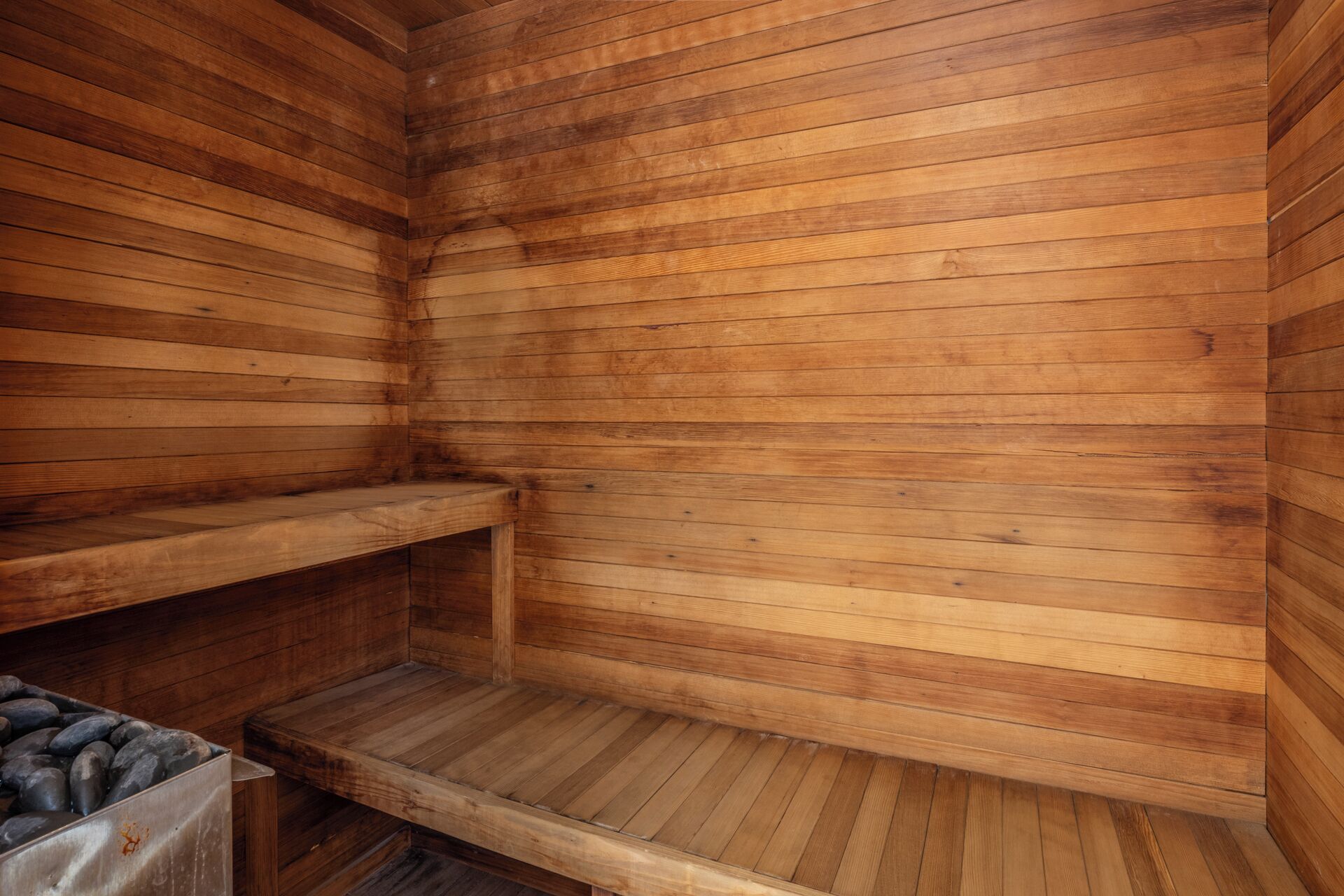 A wooden sauna with two benches and a stone basin.