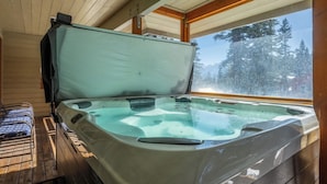 Ein Whirlpool in einer Holzhütte mit Holzinnenraum und Blick auf schneebedeckte Bäume.