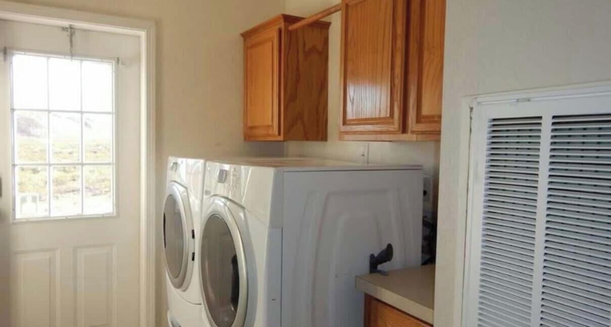 Un lavadero con lavadora y secadora de carga frontal, armarios de madera y una ventana.