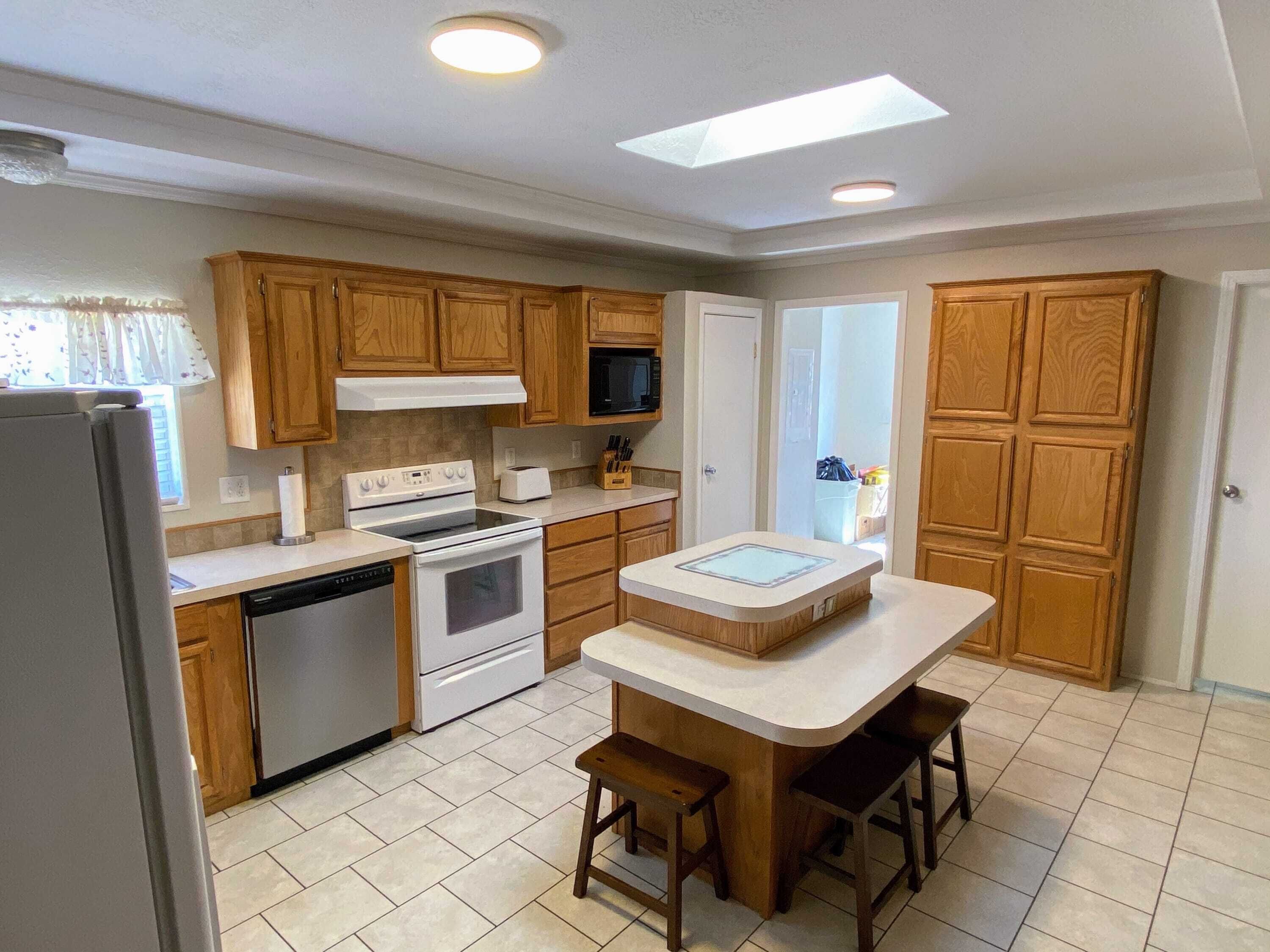 A kitchen with wooden cabinets, a central island, a dishwasher, a stove, and a microwave.