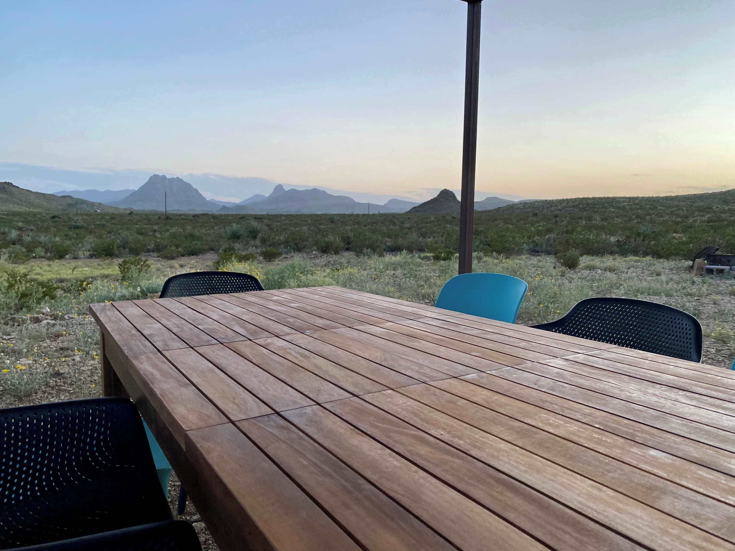 Een houten tafel met stoelen in een openlucht setting met uitzicht op bergen.