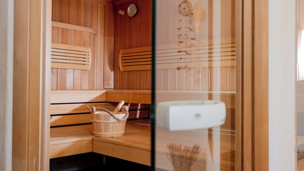 Un sauna con bancos de madera, un cubo de madera y un panel de control blanco.