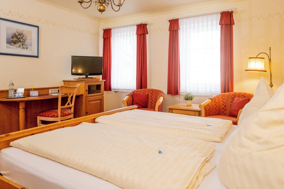 Ein Hotelzimmer mit zwei Betten, einem Schreibtisch mit Fernseher, einem Sessel und einer Lampe.