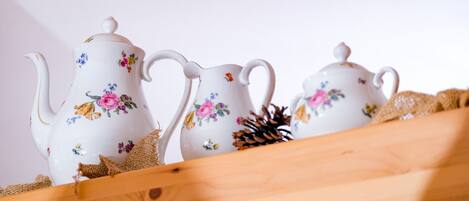 Trois théières en céramique blanche ornées de motifs floraux, posées sur une surface en bois recouverte de toile de jute et agrémentée d’une pomme de pin.